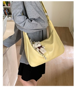 Detail of crocodile embossed yellow shoulder bag with white bear pendant and silk scarf