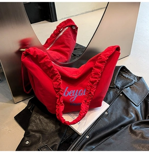 Detail of red canvas tote bag featuring ruffled shoulder straps and beyou embroidery