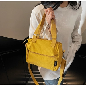 Détail d'un sac bandoulière en nylon jaune avec deux poignées et une poche zippée avant