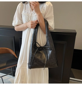 Détail d'un cabas noir en similicuir avec nœud élégant sur robe en dentelle blanche