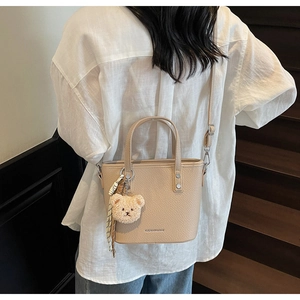 Close-up of beige leather bucket bag with bear pendant and scarf on a model