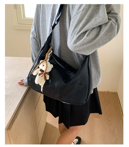 Detail of black crocodile texture shoulder bag featuring a cute white teddy bear charm