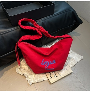 Detail of red canvas tote bag with letter print and unique pleated shoulder strap