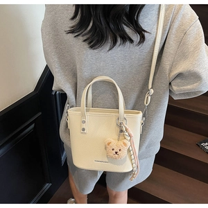 Detail of off-white tote bag with dual handles, shoulder strap and a cute bear charm