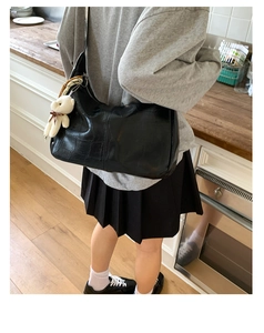 Detail of black crocodile texture hobo bag with a cute plush bear charm on the shoulder strap