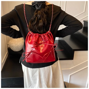 Detail view of a bright red drawstring bucket bag with decorative bows and chain strap