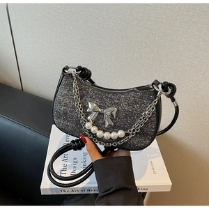 Detail of tweed underarm bag with silver bow, faux pearl strand, and metal chain accent