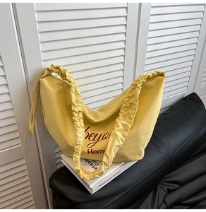 Detail of yellow canvas hobo bag with a ruched shoulder strap and red text print