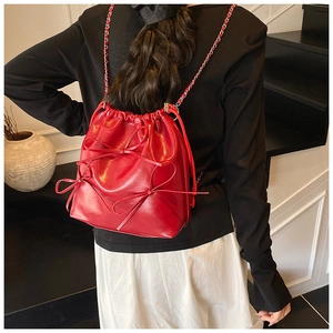 Detail of red glossy bucket bag featuring three bows and woven chain shoulder strap