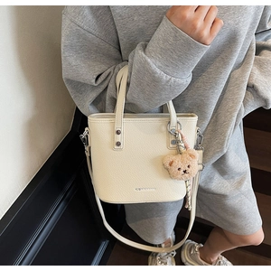 Detail of cream pebbled leather bucket bag with cute brown teddy bear charm and strap