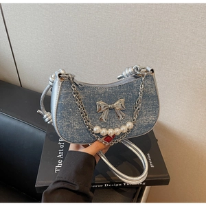 Detailed view of shimmering denim underarm bag with silver bow and pearl chain strap