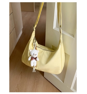 Detail of light yellow hobo bag with crocodile pattern and a cute teddy bear pendant