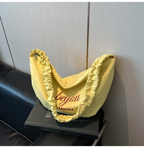 Close-up of pleated handle detail and red logo on a yellow canvas tote bag