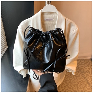 Detail of black drawstring bucket bag with leather bow and metallic chain strap