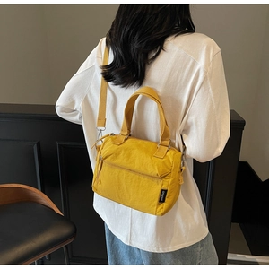 Detail of yellow nylon crossbody bag with fabric strap and metal hooks shown on model