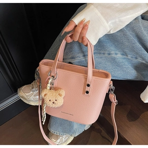 Detail of pink lychee leather tote bag with bear charm and woven rope decoration