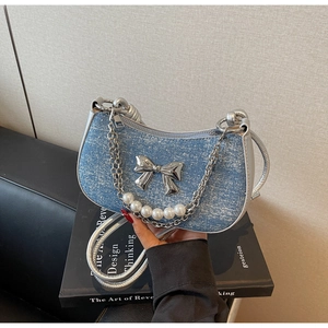 Detail of blue denim bag featuring silver bow, pearl chain and metal zipper