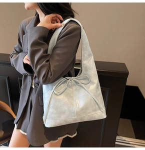 Détail du sac cabas en similicuir bleu clair avec nœud sur un blazer anthracite