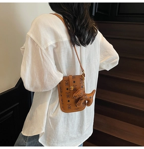 Detail of brown shoulder bag with teddy bear pattern and leather puppy charm