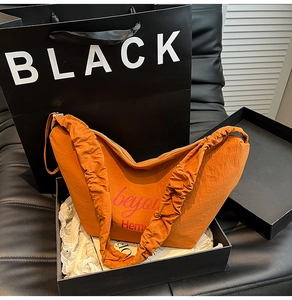 Detail of orange nylon tote bag with pleated shoulder strap in a black gift box packaging