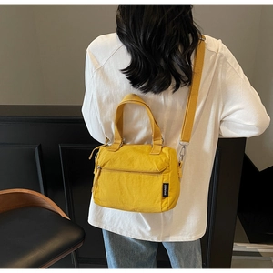 Detail of a bright yellow nylon crossbody bag with zipper pockets and top handles
