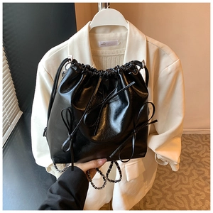 Detail of black glossy drawstring bucket bag with bow accents and silver chain strap