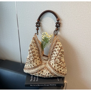 Detail of woven straw tote with wooden bead handles on a black leather surface