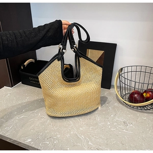 Détail du sac cabas en paille tressée avec lanières en cuir noir et anneaux dorés