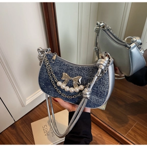 Detail of blue denim underarm bag featuring silver bow, pearls, and metallic chain strap