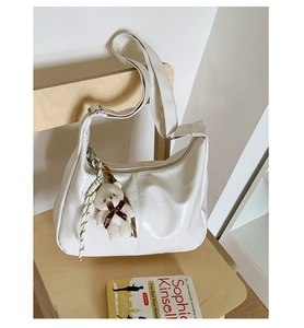 Detail of white croc-effect crescent bag with a cute plush bear charm on a wooden chair
