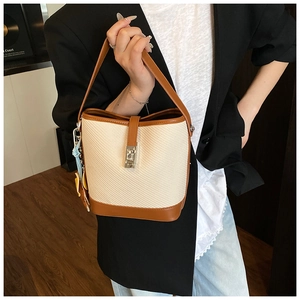 Detail of beige woven bucket bag with brown leather trim and silver metal twist lock