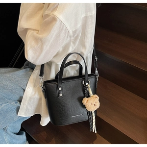 Detail of black pebbled leather bucket bag with top handles and cute bear pendant charm