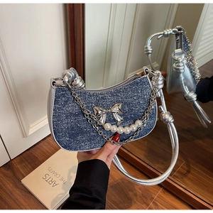 Close-up of blue denim handbag featuring a silver bow, pearl chain and metal handle