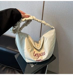 Detail of cream pleated canvas tote with red beyou text and textured nylon material