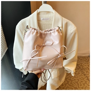 Detail of light pink bucket bag featuring decorative bows and metal chain strap