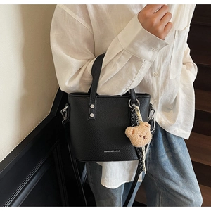 Detail of black lychee grain bucket bag with silver studs and a plush bear charm
