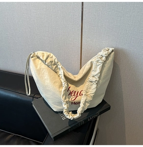 Detail view of cream pleated shoulder bag with red lettering and textured fabric finish