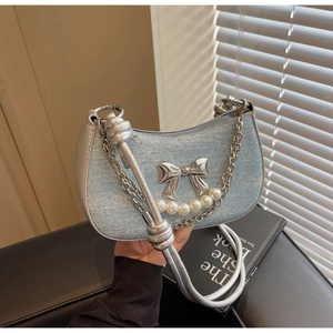 Detailed view of light blue denim crescent bag with pearl and silver bow accents