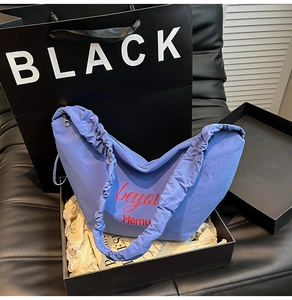 Close-up of blue crescent canvas tote with pleated handle inside black gift box