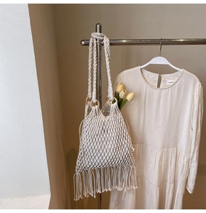 Detail of cream woven bucket bag with long tassels and decorative wooden ring handles