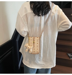 Close-up of cream crossbody bag with teddy bear pattern and white dog charm detail