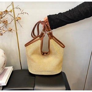 Détail du sac cabas en paille avec anses en cuir marron sur un banc moderne