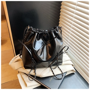 Detailed shot of black glossy drawstring bucket bag with decorative bows and chain strap
