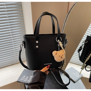 Detail of black pebbled leather bucket bag with bear charm and silk scarf decoration