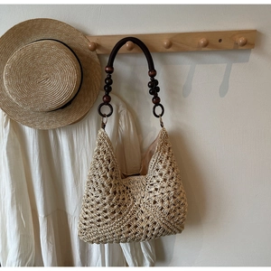 Detail of hollow straw tote bag with brown wooden bead shoulder strap in a rustic setting