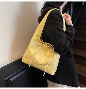 Détail d'un sac porté épaule jaune gingembre avec nœud sur un blazer noir élégant