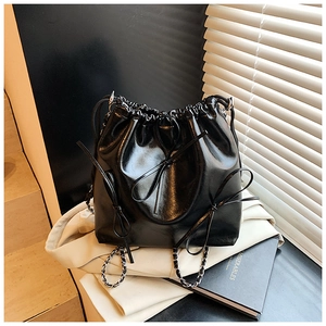 Detail view of black drawstring bucket bag with shiny finish and silver chain strap
