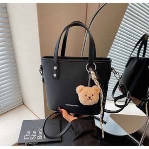 Detail of black lychee leather bucket bag with bear charm and floral silk scarf