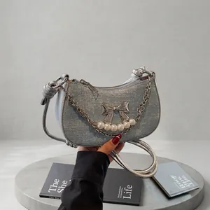 Detail of light blue denim crescent bag with silver bow and pearl accents