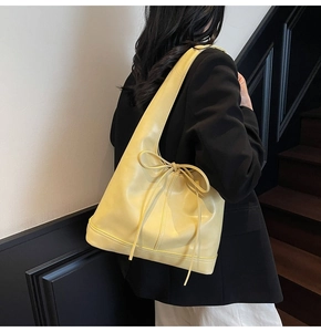 Détail d'un sac hobo jaune avec nœud porté par un mannequin en blazer noir